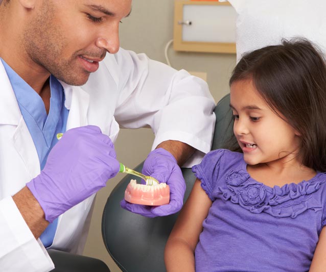 dentist explaining how to clean teeth to a little girl