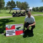 dentist posing next to a Hole-in-One Win Vehicle sign